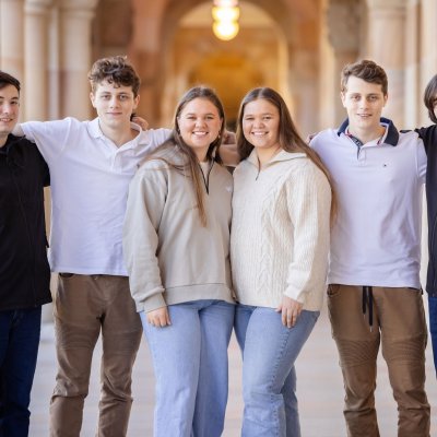 a group of six people stand in a corridor with their arms around each other